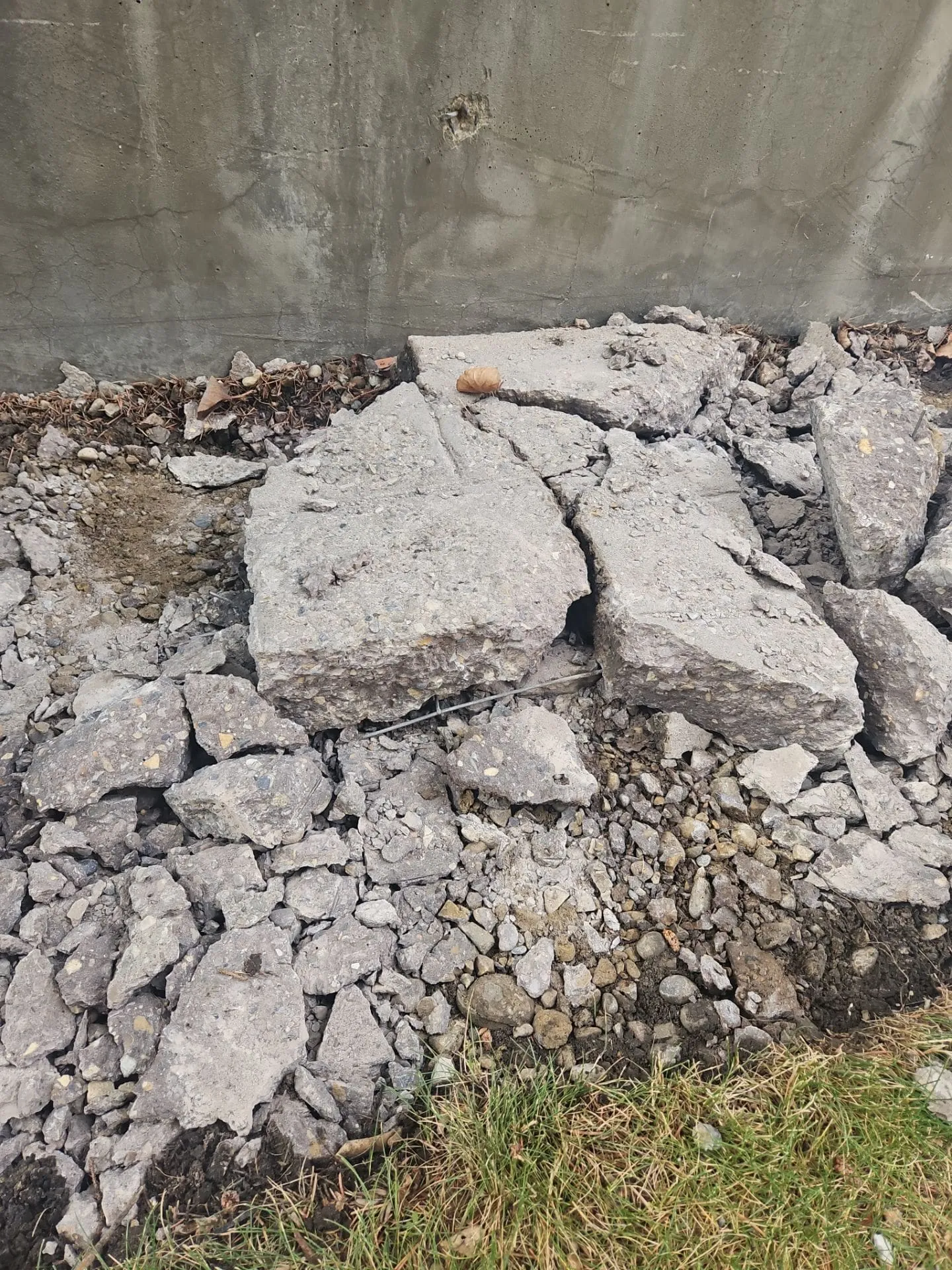 Broken concrete chunks piled against a foundation wall during removal at 15304 Bannister Rd SE, Calgary