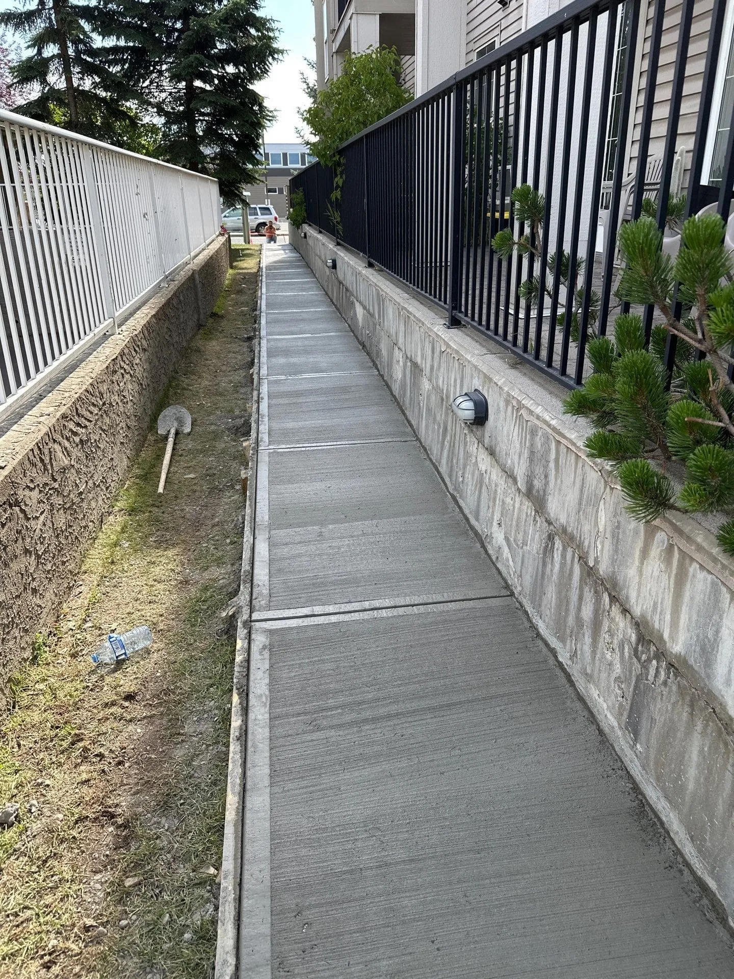 Broom-finished concrete sidewalk running between a white railing and a retaining wall