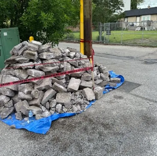 Broken-up concrete piled on a tarp behind caution tape, staged for haul-away