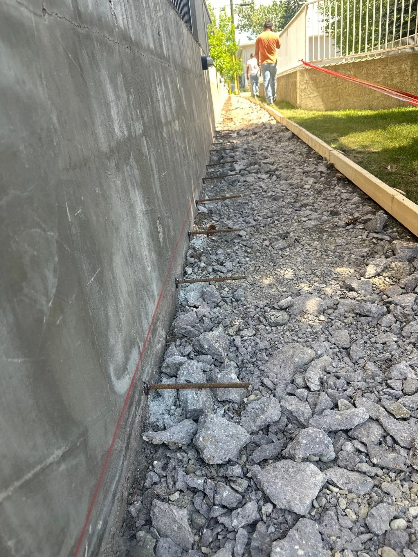 Row of rebar dowels drilled along retaining wall with forms set for sidewalk pour at the Solea Building in Calgary